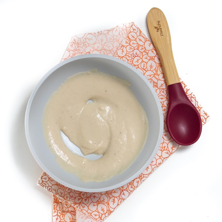 Gray baby bowl with chicken puree inside with spoon resting next to the bowl. 