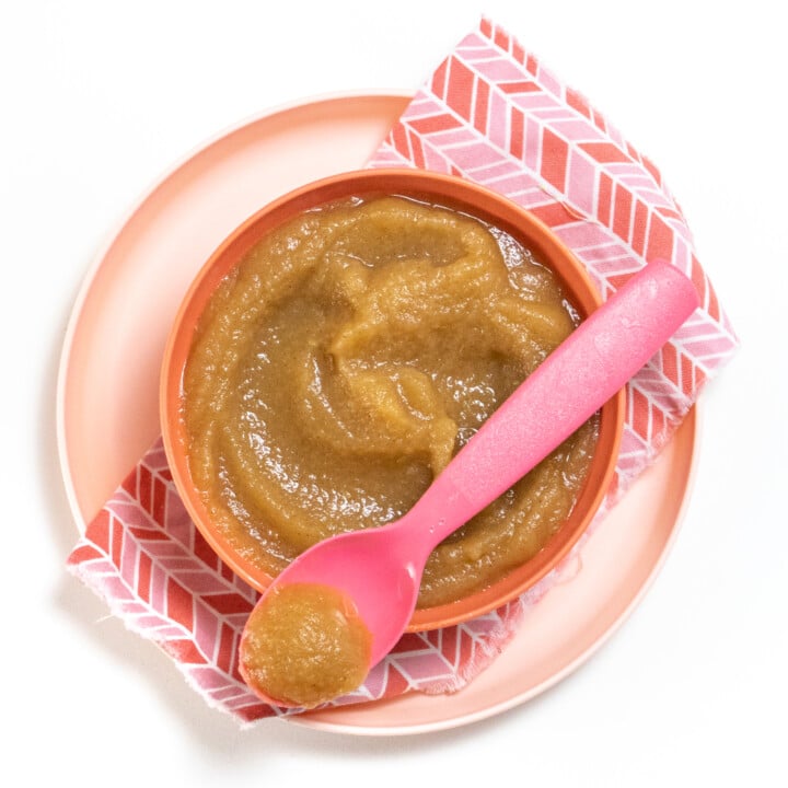 Pink kids bowl full of homemade applesauce with a pink kids spoon full as well with applesauce.