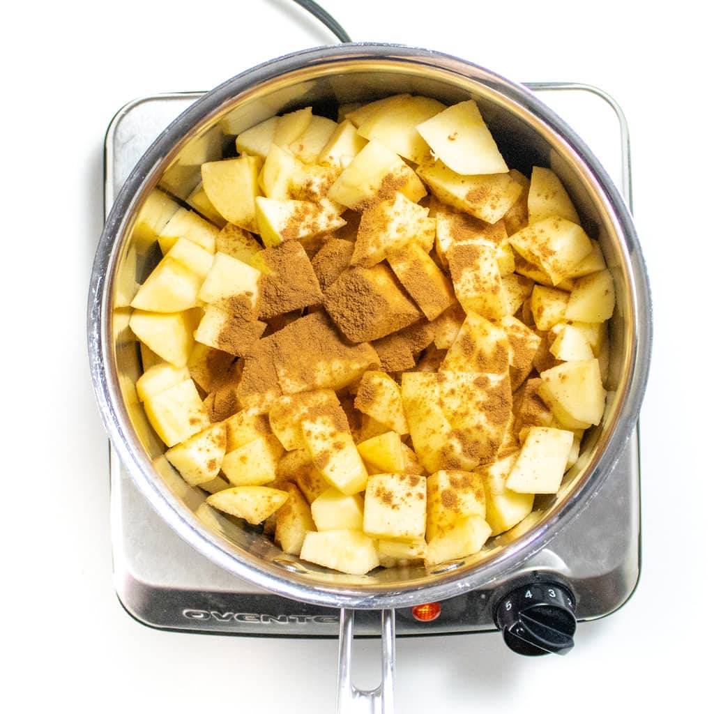 Silver saucepan on a burner with chopped apples, cinnamon and vanilla, getting ready to be simmered.