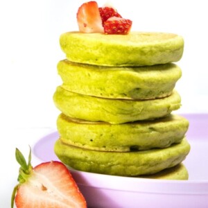 A stack of spinach pancakes against a white background with strawberries on top and on the side.