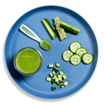 Blue baby plate showing different ways for different ages to serve cucumbers to baby. On a white countertop.