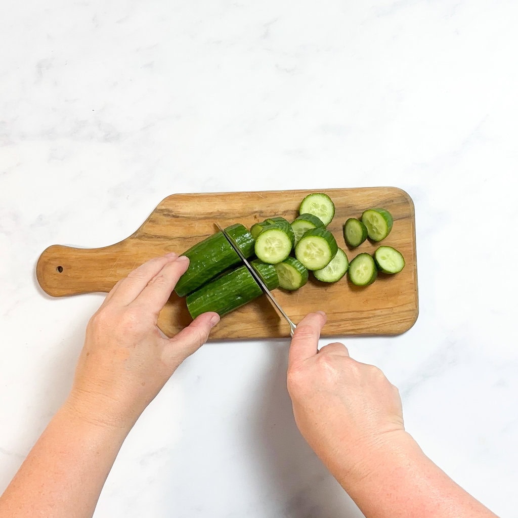 I'm cutting up three cucumbers into slices for a baby food purée on a white kitchen counter in my kitchen.