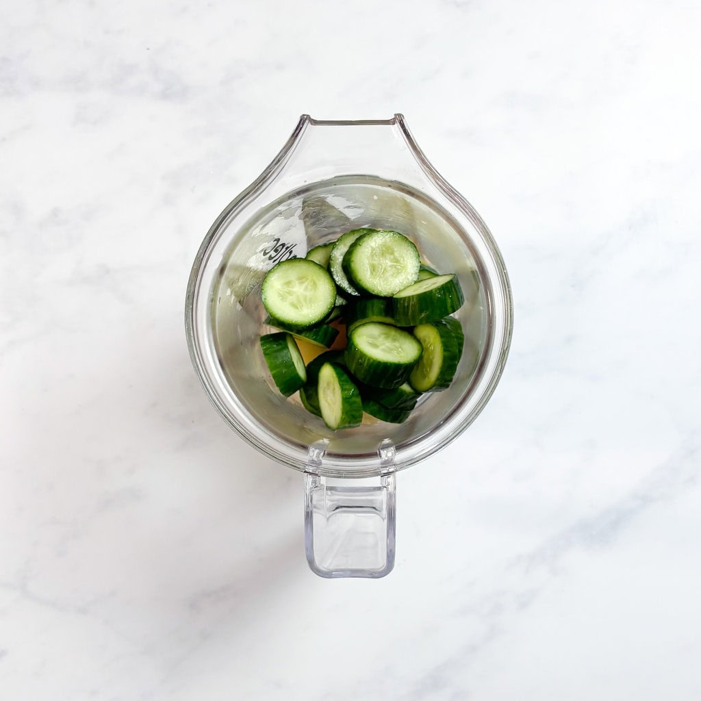 A clear blender on my white kitchen counter. The blender is full of steamed pears and sliced cucumbers.