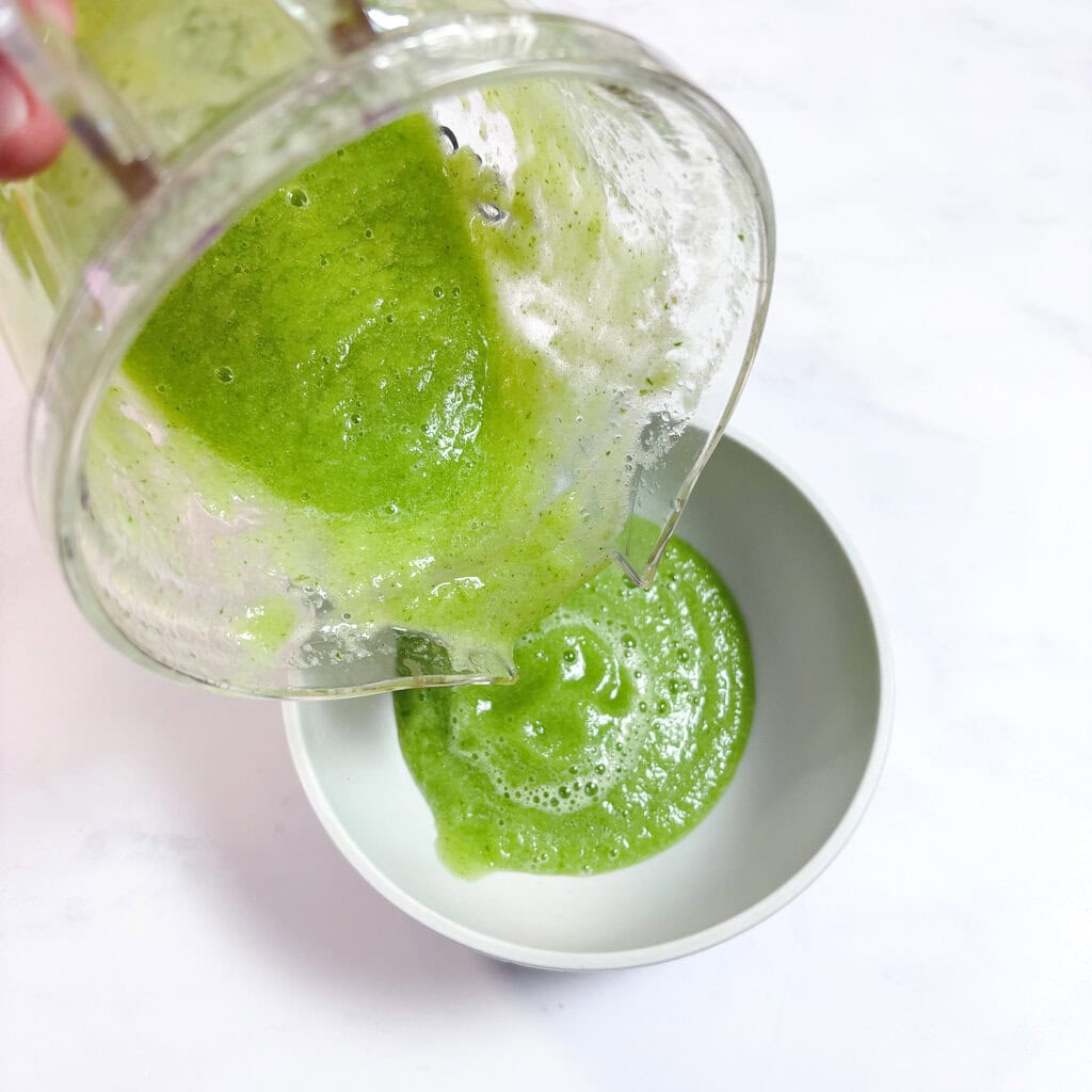 A cucumber purée being poured into a gray bowl on a white kitchen counter.