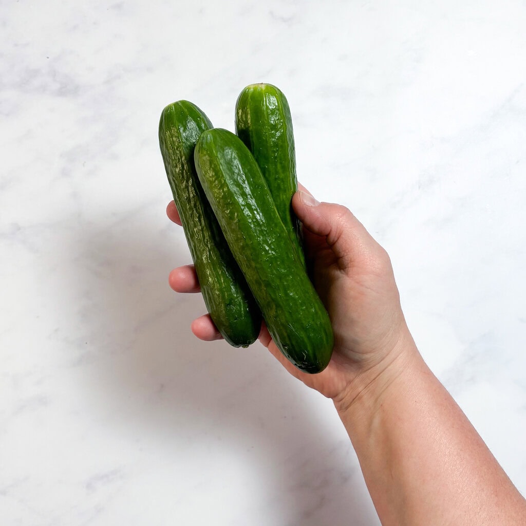 A hand holding three cucumbers in my kitchen over a white countertop.