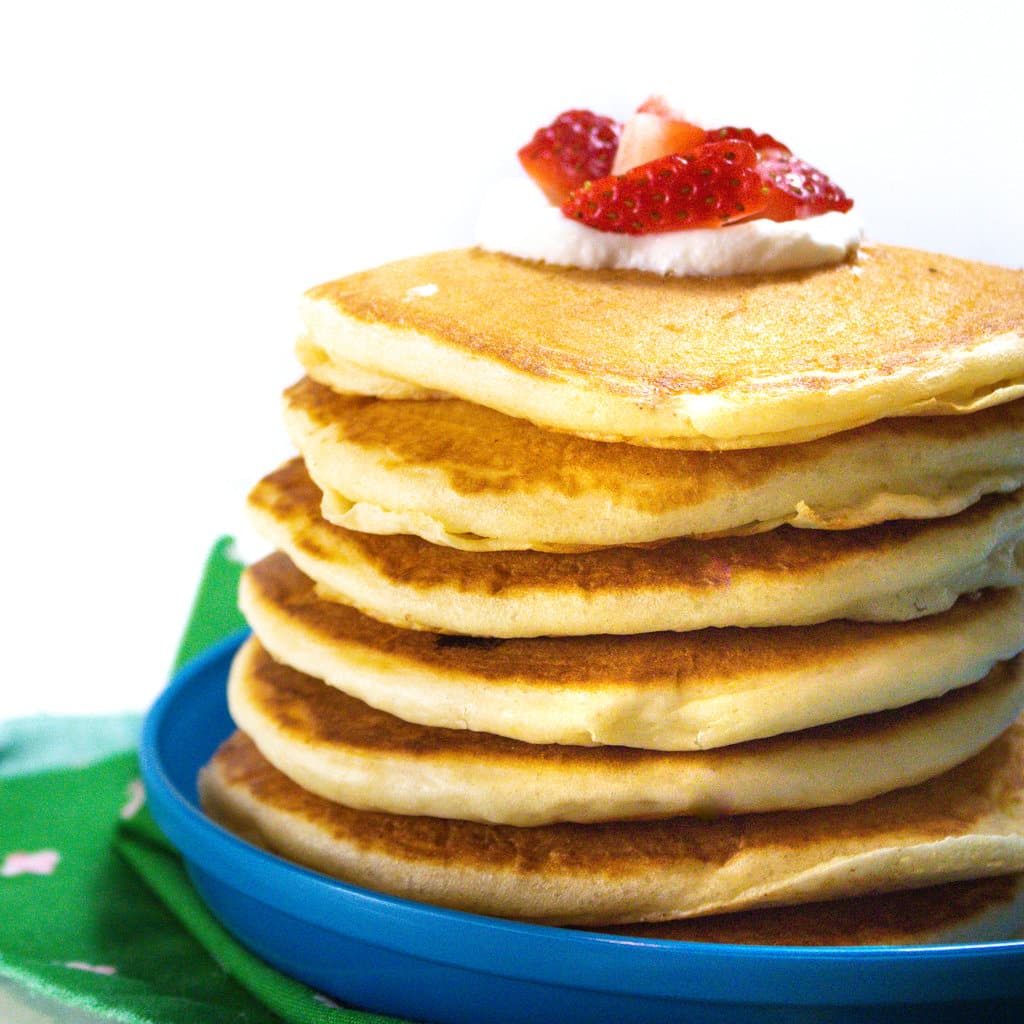 Side view of a stack of yogurt pancakes with yogurt and strawberries on top sitting on a blue kids plate.