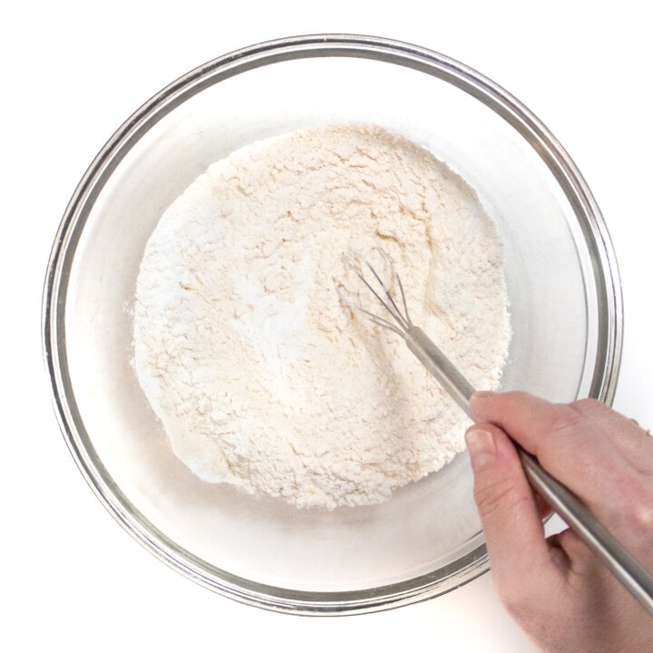 Clear mixing bowl with her hands stirring the dry ingredients for yogurt pancakes.