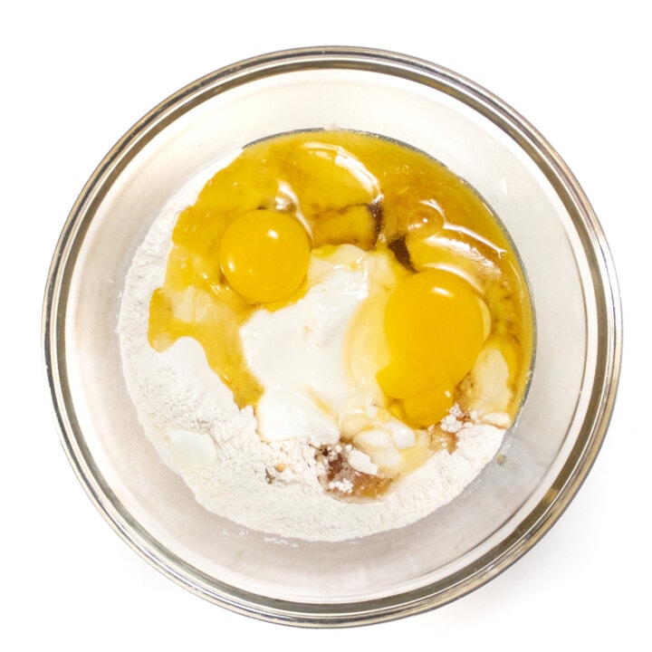 A clear mixing bowl with the wet ingredients and the dry ingredients about to be mixed into a batter for yogurt pancakes.