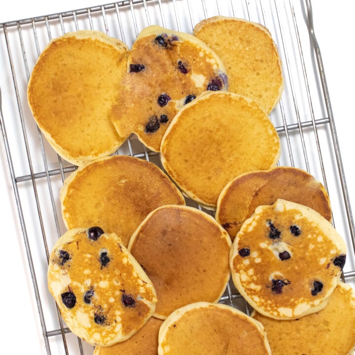 A cooling rack against a white background on top of the cooling rack are yogurt pancakes some with blueberries.