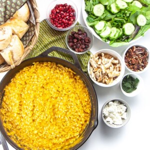 Spread of food on a counter will a big saucepan full of pumpkin risotto.