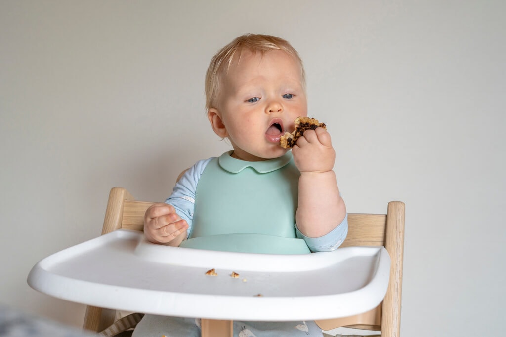 baby in highchair eating food with his own hands.