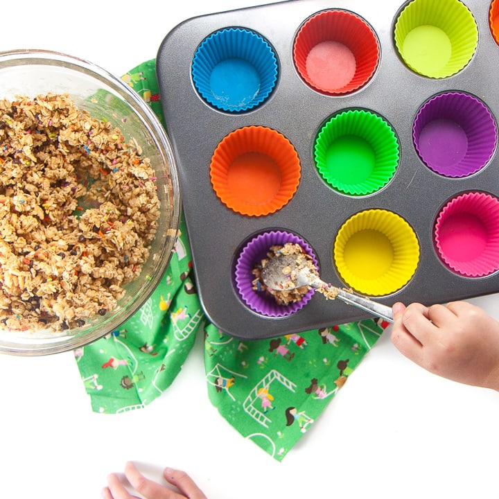 Kid scooping granola into muffin liners.