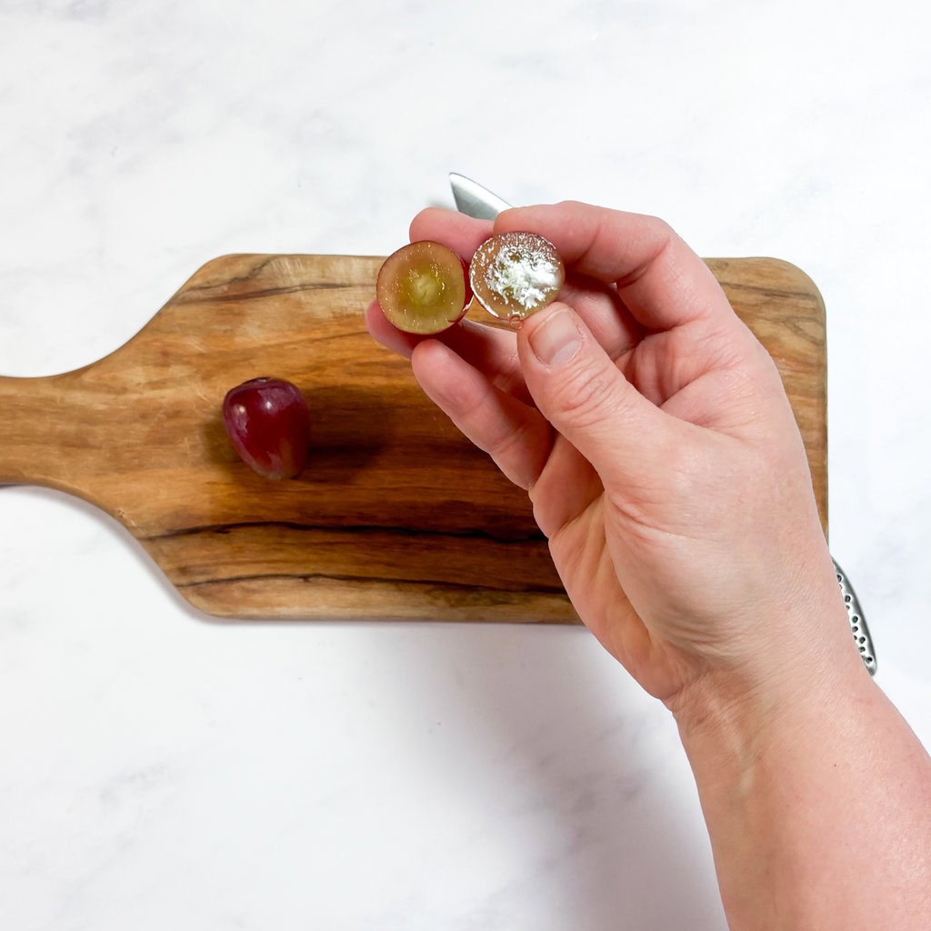 A handholding grapes cut down the middle showing how not to cut grapes for your baby.