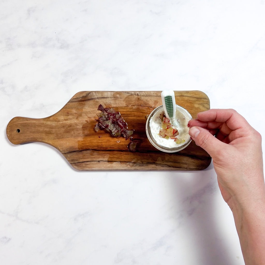 A hand putting mashed grapes into a glass jar with yogurt.