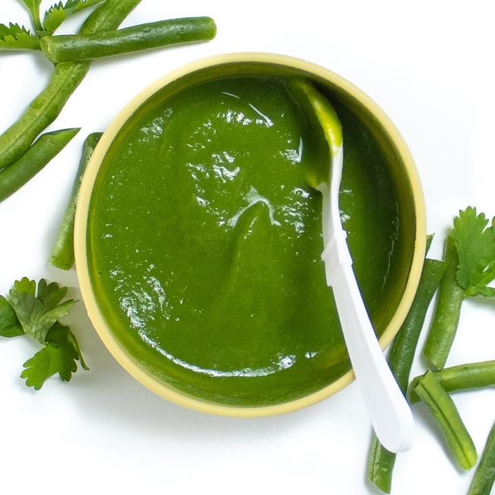 Green bean puree in a bowl with produce surround it.