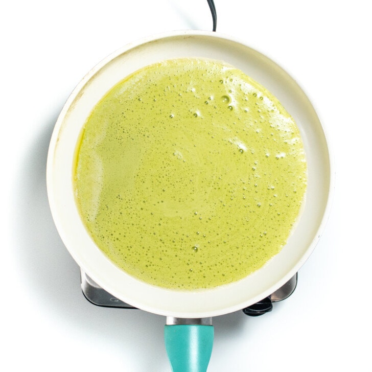 A skillet with blended spinach and eggs being cooked on a white countertop.