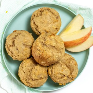 Teal blue plate with a stack of apple muffins and a side of sliced muffins sitting on a blue napkin on a white counter.