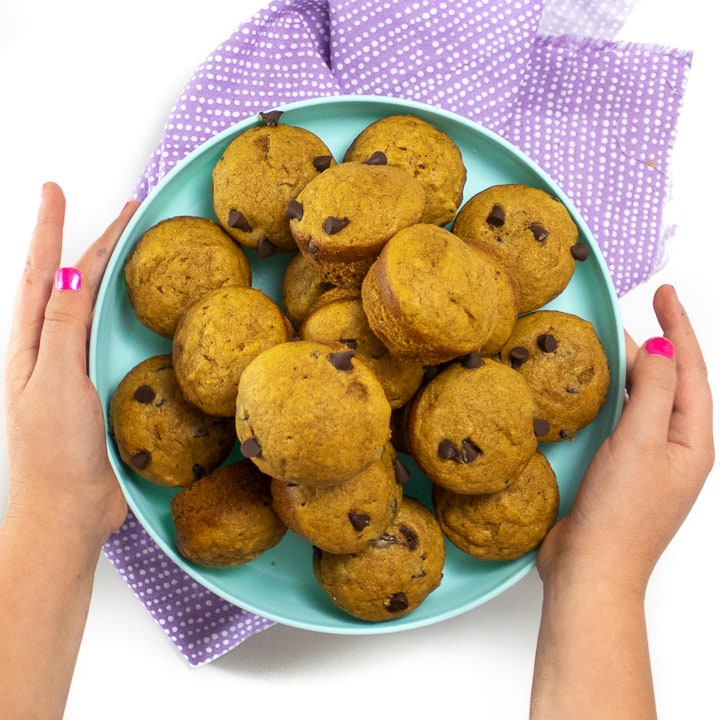 Small kids hands holding a plate of mini pumpkin muffins.