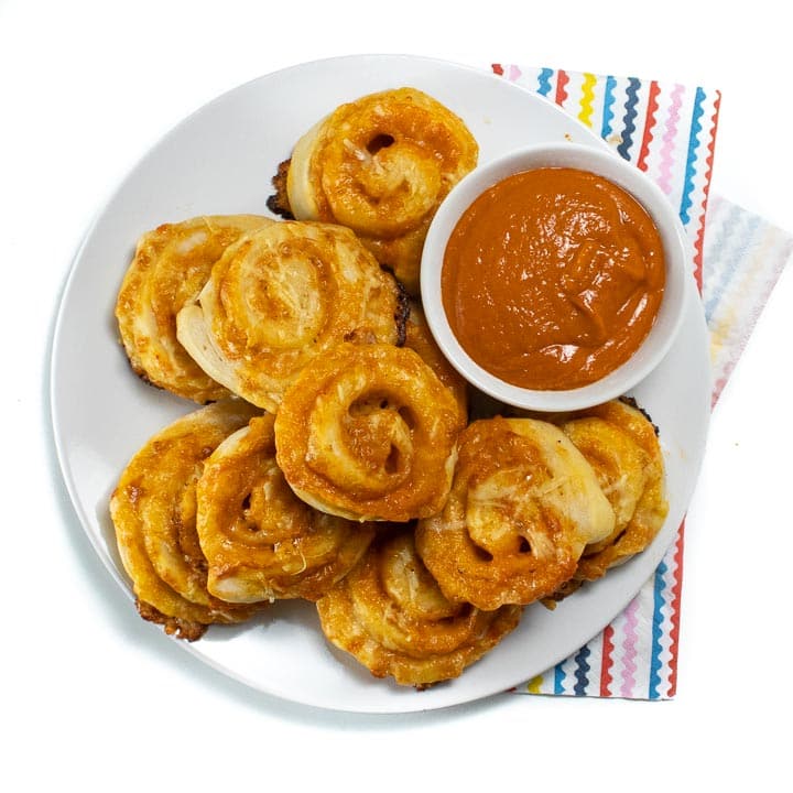 Plate of veggie hidden pizza rollups with a side of sauce ready for kids to take and eat.