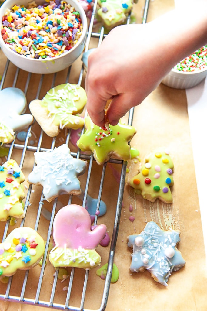 Small hand decorating gluten free sugar cookies with sprinkles.