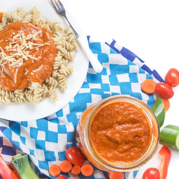 A plate of cooked pasta, with a jar of hidden veggie pasta sauce.