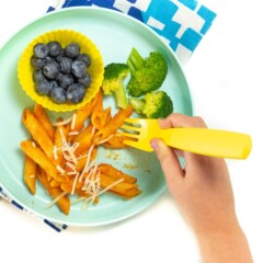 Small kids hands eating off a plate with hidden veggie pasta sauce with pasts, blueberries and broccoli.