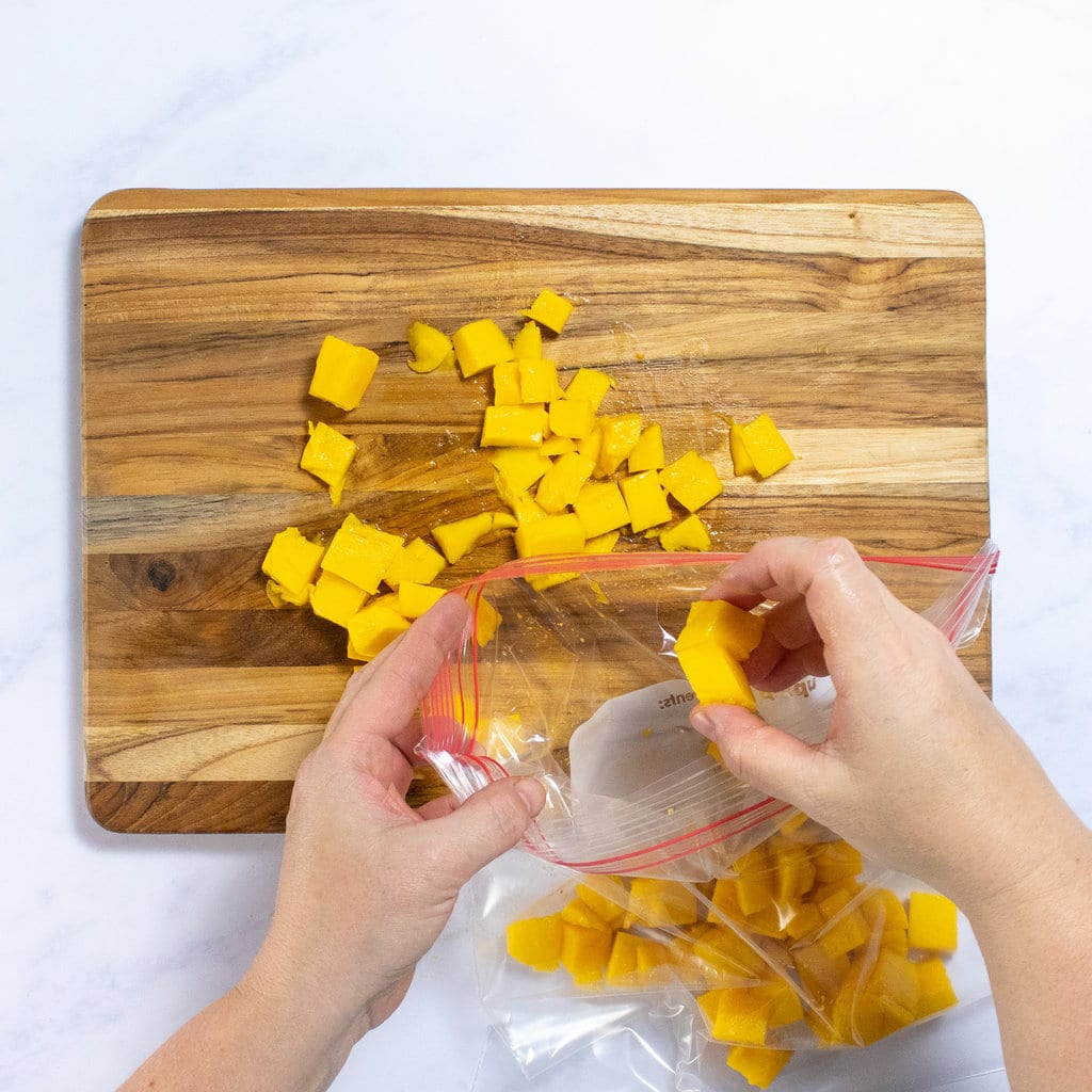 Hands putting mango chunks into a bag.