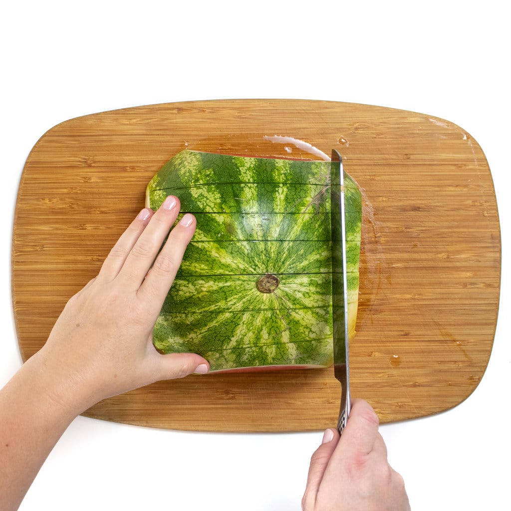 Hands holding a knife cutting a watermelon into long sticks