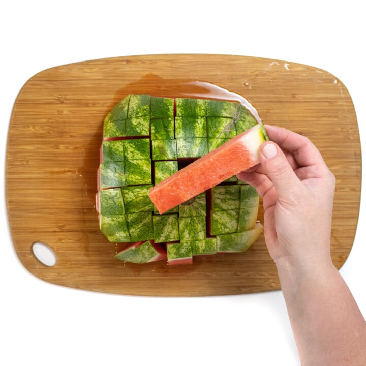 A hand holding and showing off a 6 inch watermelon stick over the rind of the watermelon.