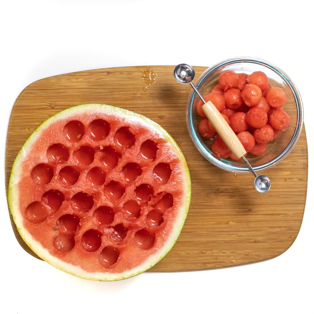 They have a watermelon with holes in it in a bowl of melon balls sitting next to it.