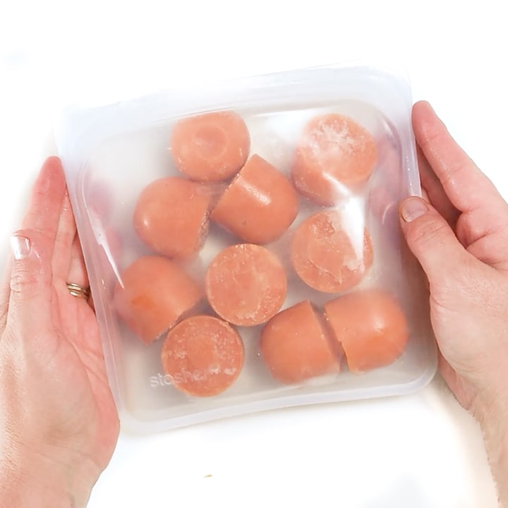 Hands holding a stasher bag of frozen baby food puree.