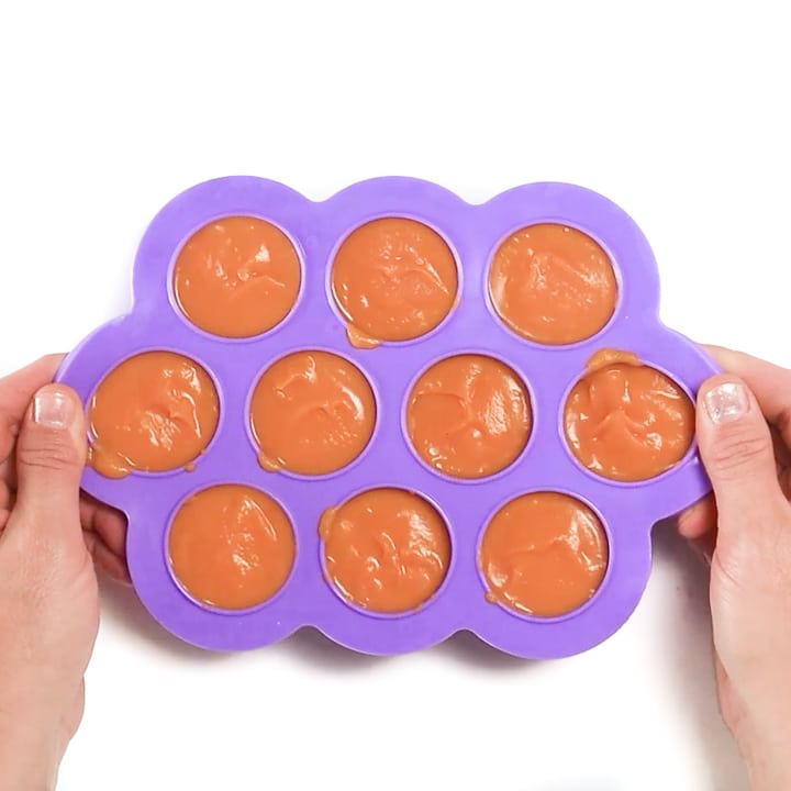 Hands holding a tray of homemade baby food puree.