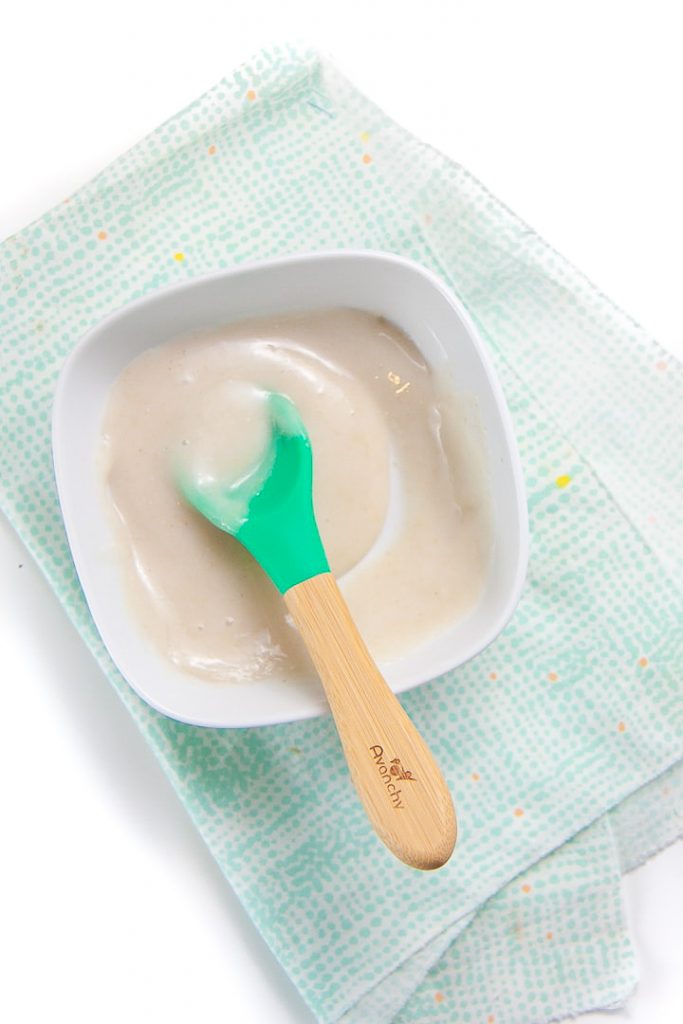 White bowl filled with homemade baby rice cereal with teal spoon inside.