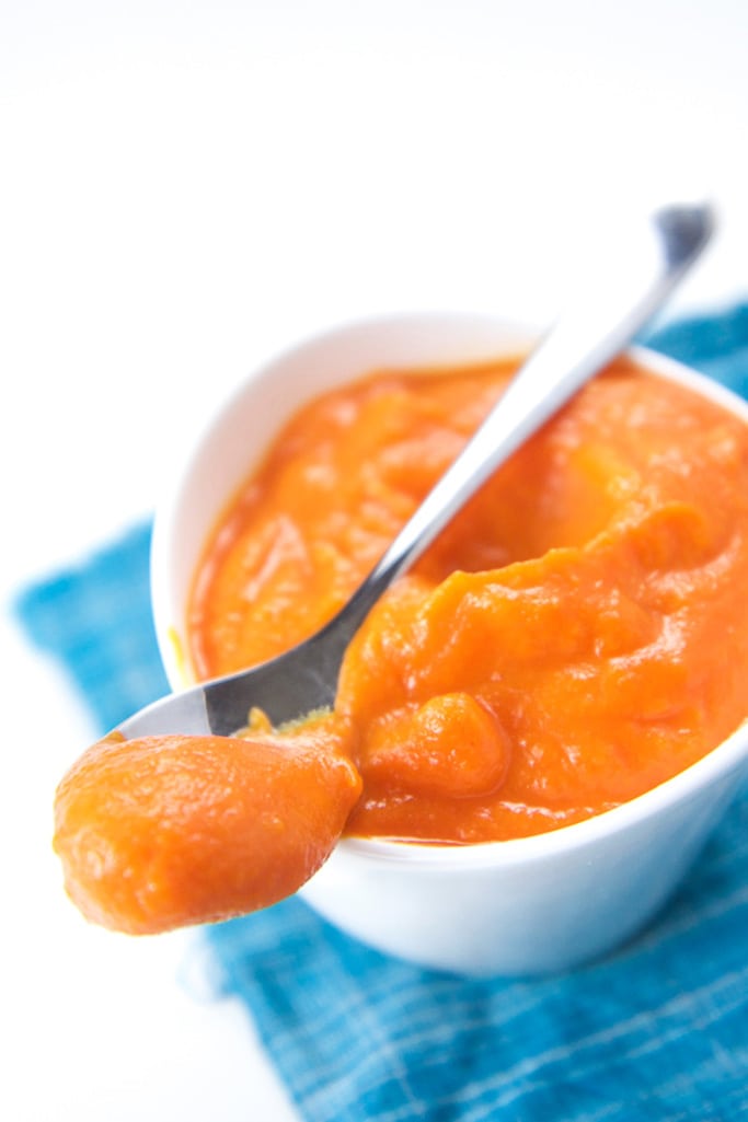 A small white bowl filled with a thick and bright colored baby food puree.