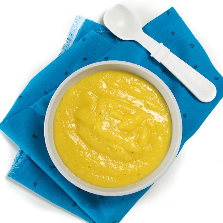 Bowl of mango baby food puree on a blue napkin.