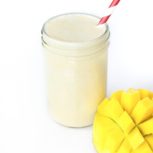 A clear glass full of mango back with a red straw and pieces of mango next to it.