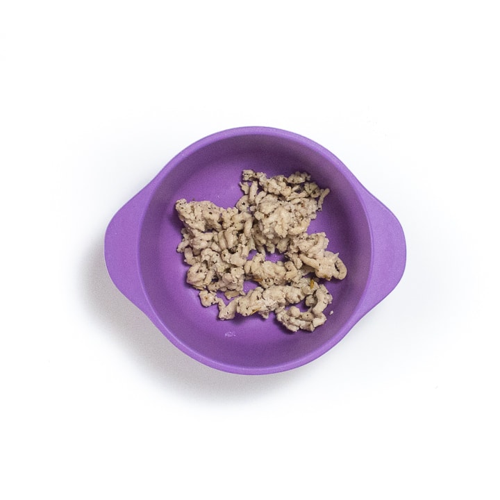 Hand holding a purple baby bowl filled with cooked ground chicken