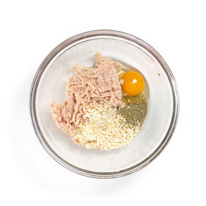 Clear mixing bowl full of ingredients for meatballs.