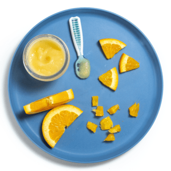 Blue baby plate with different ways to serve oranges to your baby on a white countertop.