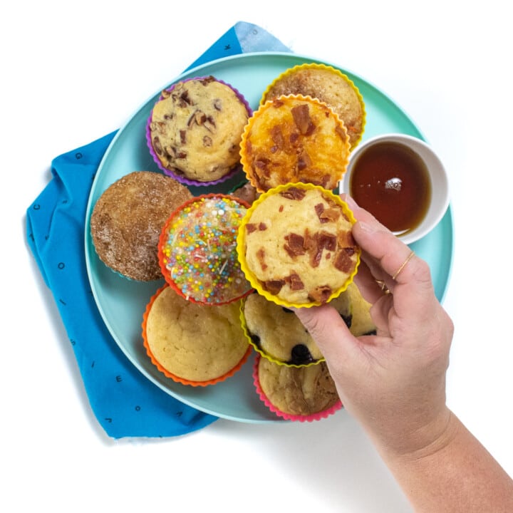 A blue kids play with the blued kids napkin, the plate has pancake muffins with various toppings.