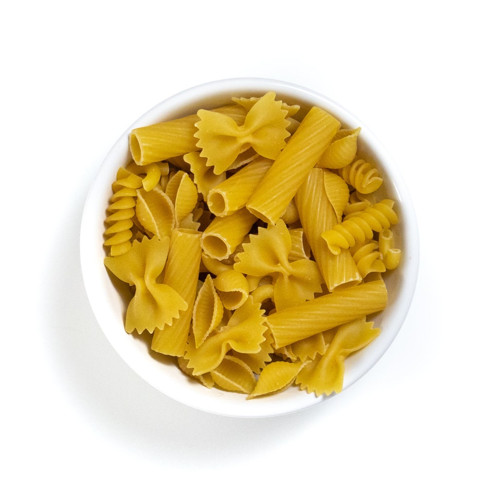 white bowl against a white background filled with a ton of different shaped pasta.