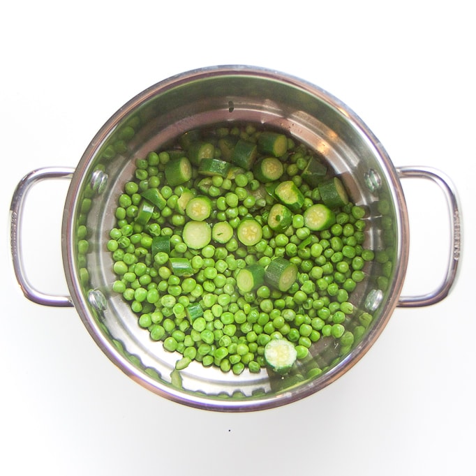 Silver steamer basket filled with steamed peas and zucchini. 