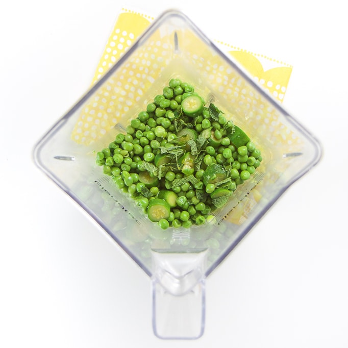 Clear blender filled with steamed peas and zucchini and a pinch of mint.