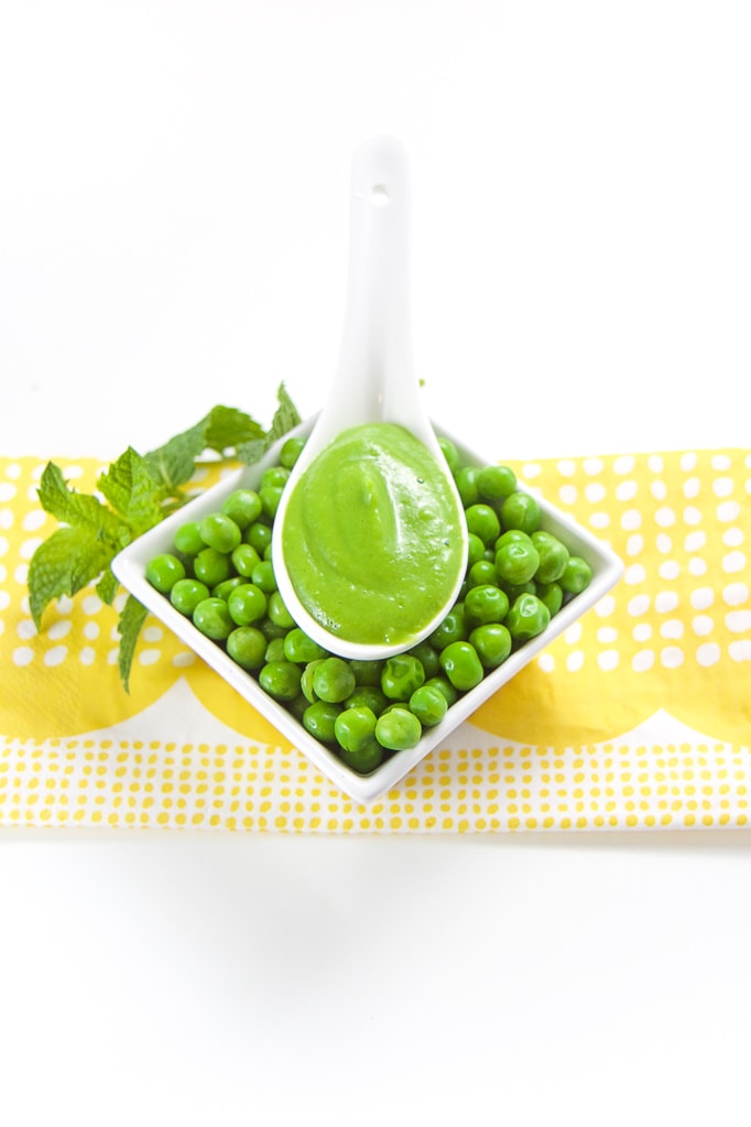 Pea puree sitting on a tray of fresh peas with mint tucked behind it. 