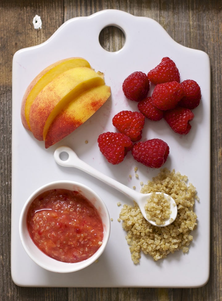 White cutting board with a spread of produce and a small bowl filled with a chunky baby food puree.