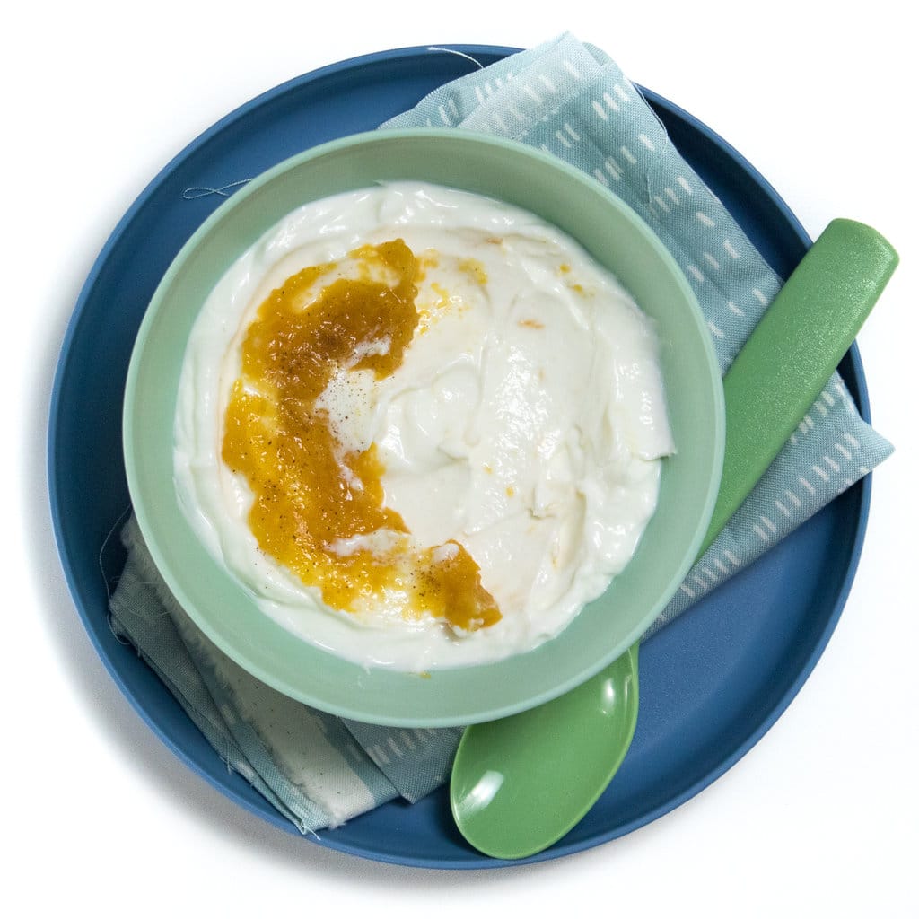 A blue plate and kids green bowl with a green spoon full of peach yogurt.