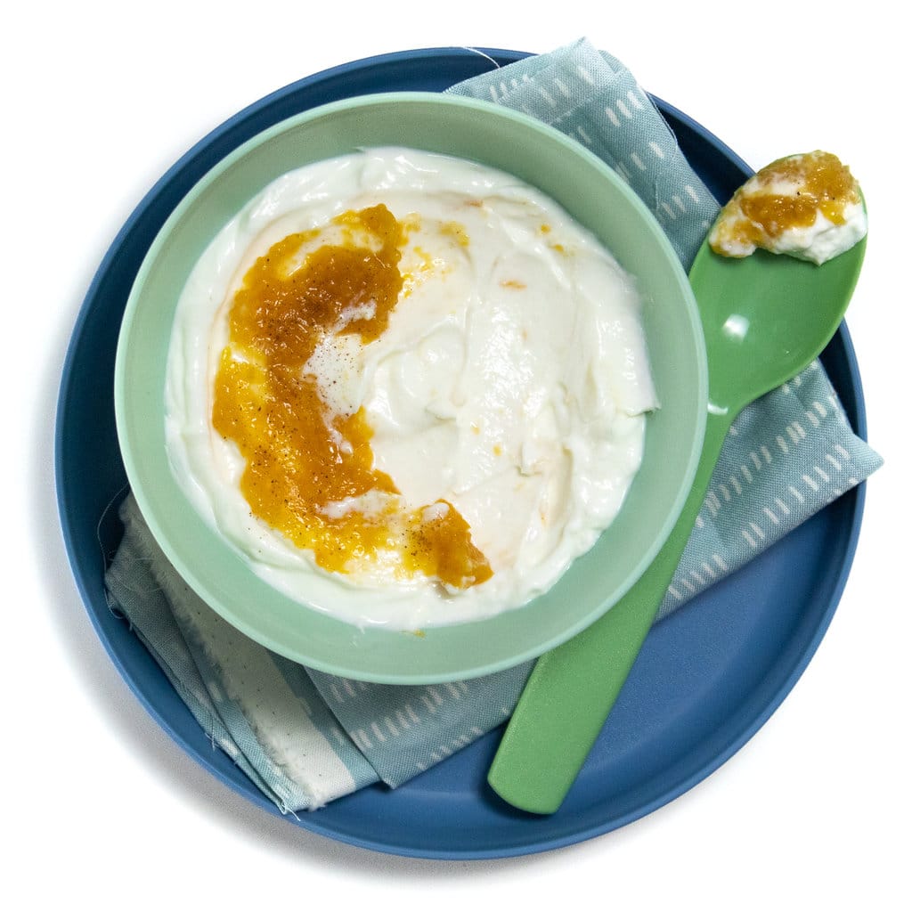 A blue plate and kids green bowl with a green spoon full of peach yogurt.