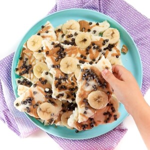 small hand reaching for a piece of peanut butter banana frozen yogurt bark.