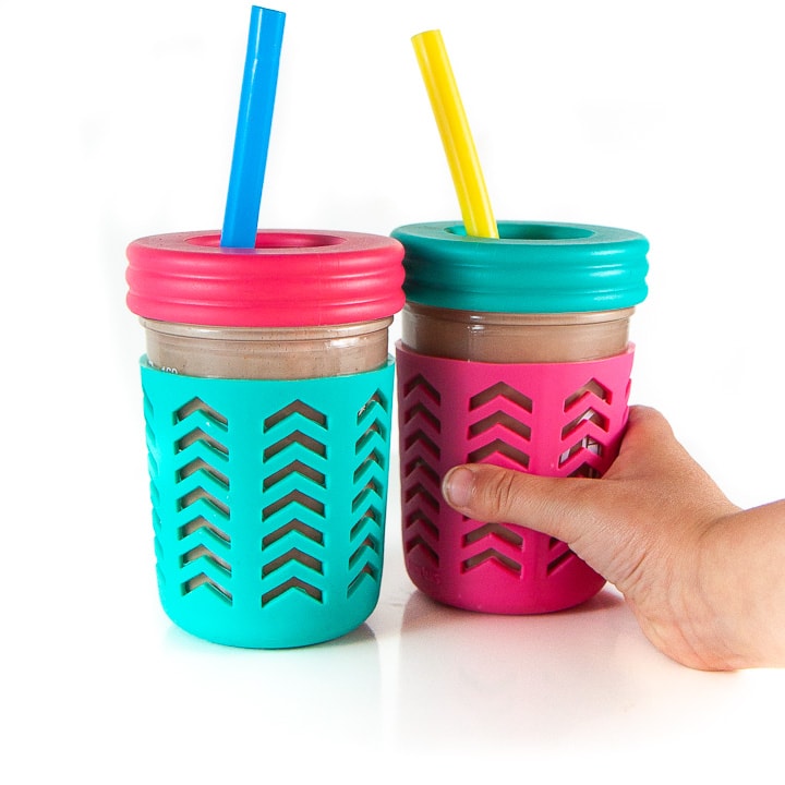 2 smoothie cups with a small kids reaching towards one of the cups.