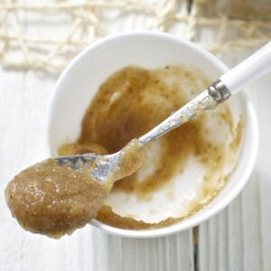 Small white bowl with a baby spoon resting on top filled with baby food.